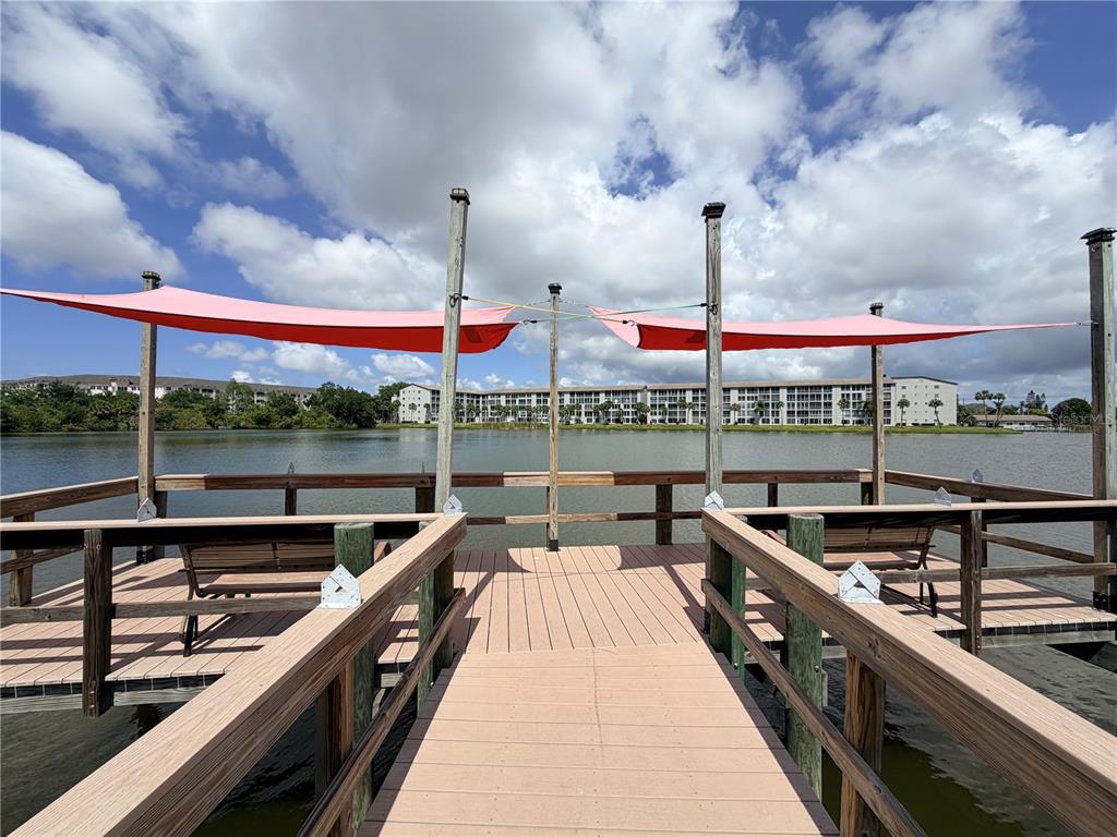 A wooden pier with pink shade sails overlooks a lake and a large apartment building — 3621 LAKE BAYSHORE DRIVE UNIT J-403, BRADENTON, FL