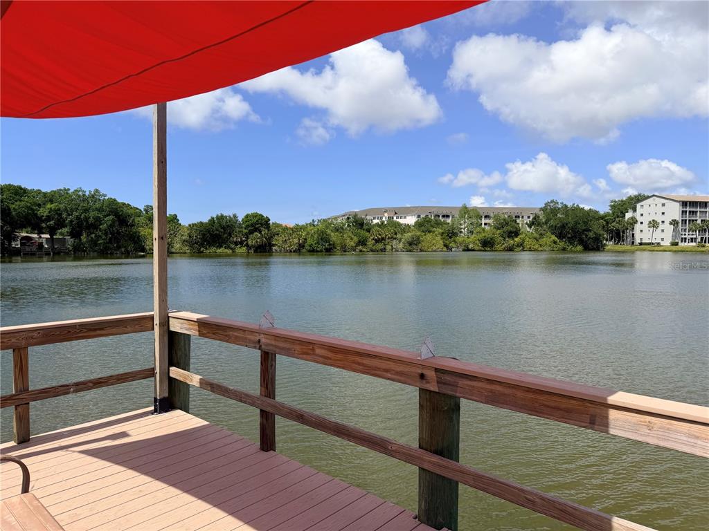 A wooden deck with a red canopy overlooks a lake and distant apartment buildings — 3621 LAKE BAYSHORE DRIVE UNIT J-403, BRADENTON, FL