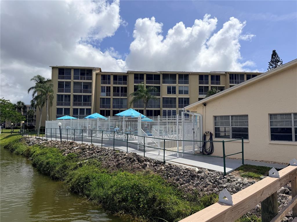 A multi-story apartment building sits behind a fenced pool area next to a pond — 3621 LAKE BAYSHORE DRIVE UNIT J-403, BRADENTON, FL