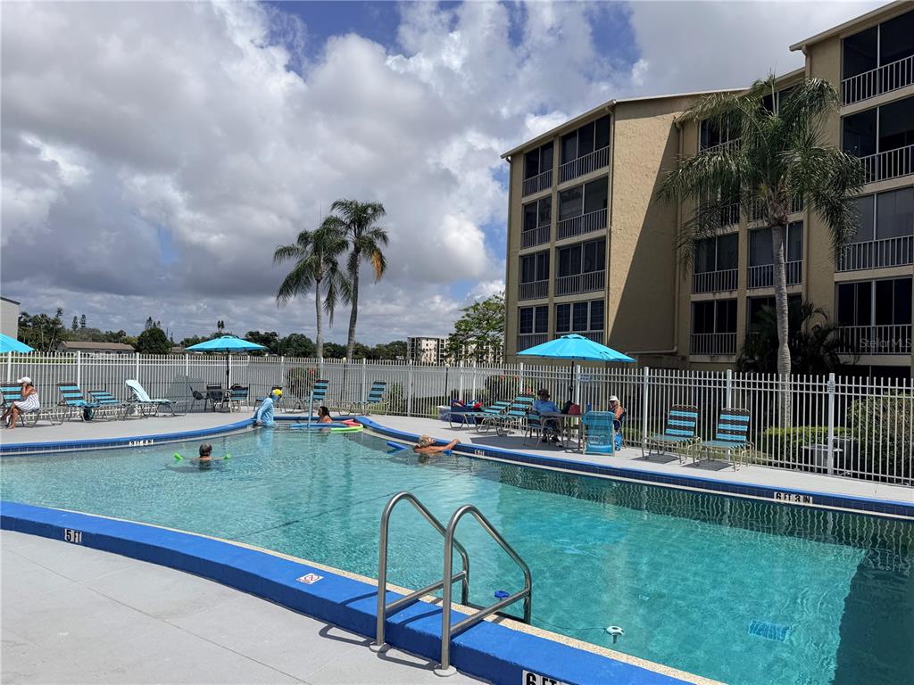 A swimming pool with lounge chairs and umbrellas sits beside a multi-story apartment building — 3621 LAKE BAYSHORE DRIVE UNIT J-403, BRADENTON, FL