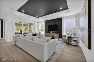 A living room features a tray ceiling, a dark accent wall with a television, and furniture — 331 FISHTAIL PLACE, PALM COAST, FL