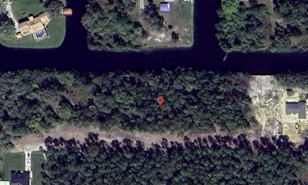 This is a satellite map view showing a wooded, undeveloped residential lot along a canal — 1122 POINCIANA DRIVE, INDIAN LAKE ESTATES, FL