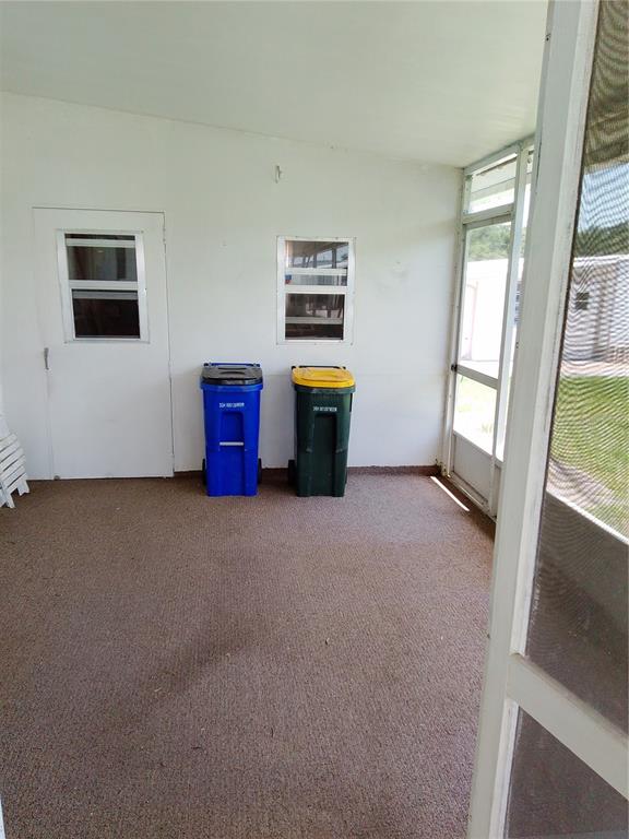 A screened-in porch with brown carpet, white walls, a door, a window, and two trash bins — 2904 LAS VEGAS BOULEVARD, SEBRING, FL