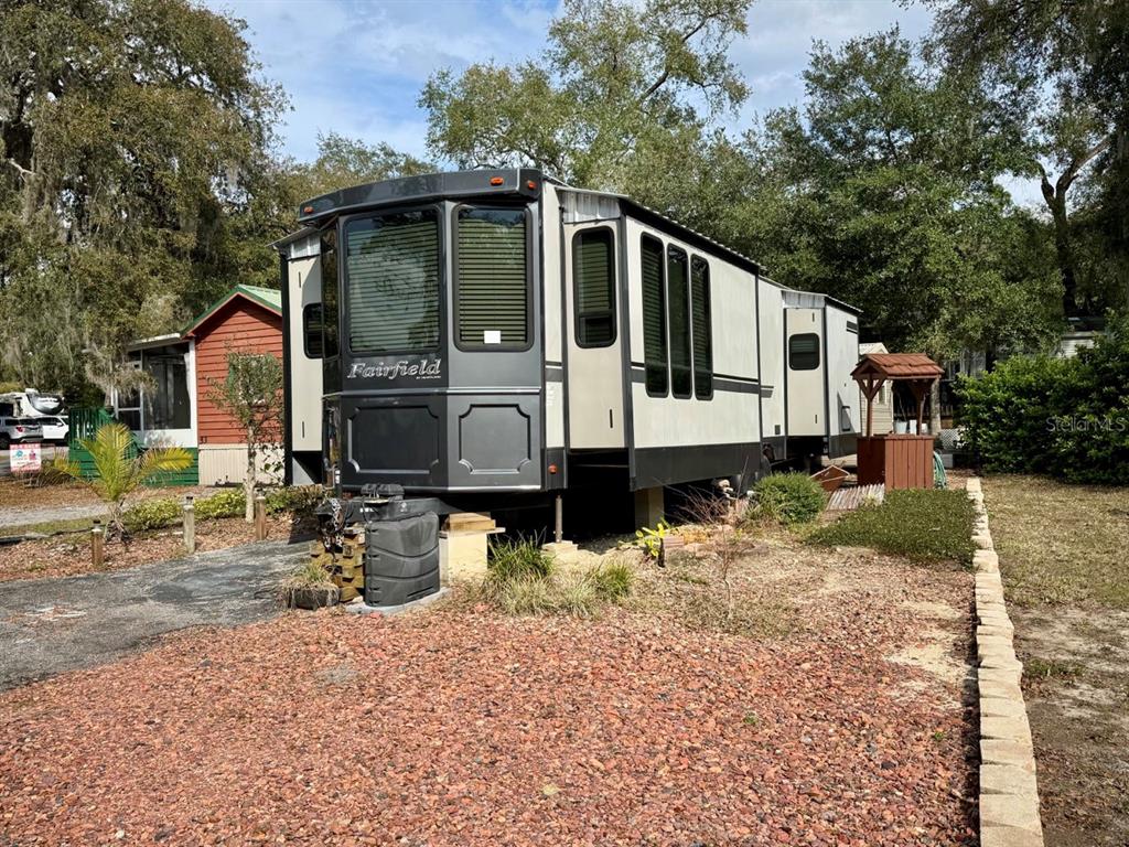 A Fairfield park model trailer sits on a gravel lot next to a small wishing well — 25132 NE 143RD STREET UNIT 52, FORT MC COY, FL