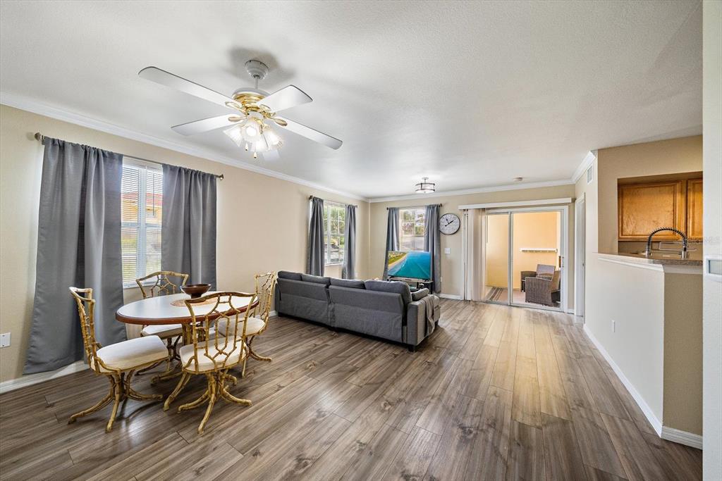 An open-concept living and dining area features wood-look flooring, a ceiling fan, and sliding doors — 1010 VILLAGIO CIRCLE UNIT 104, SARASOTA, FL