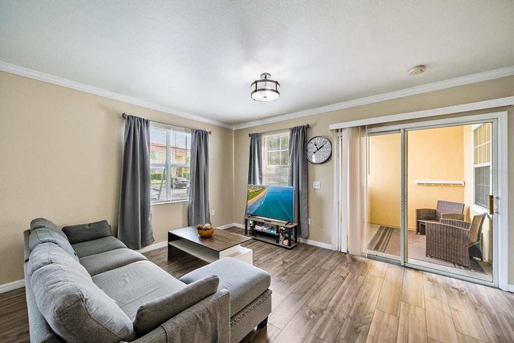 A living room features a gray sectional sofa, wood-look flooring, and a sliding glass door — 1010 VILLAGIO CIRCLE UNIT 104, SARASOTA, FL