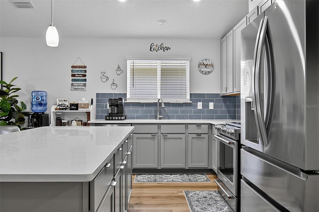A modern kitchen features gray cabinets, a white island, stainless steel appliances, and blue backsplash — 7 SIGNET COURT, FLAGLER BEACH, FL