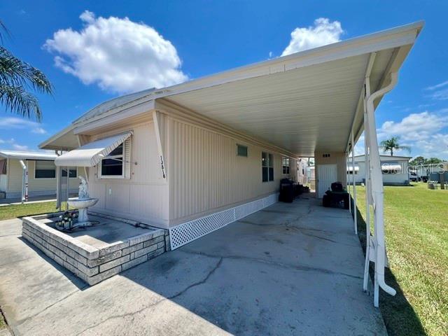 A light-colored mobile home features a large attached carport and a small stone-walled garden area — 10818 FREEDOM DRIVE, PORT RICHEY, FL