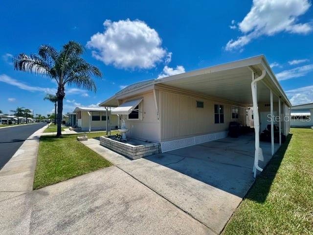 A light-colored mobile home features a large attached carport and a palm tree nearby — 10818 FREEDOM DRIVE, PORT RICHEY, FL