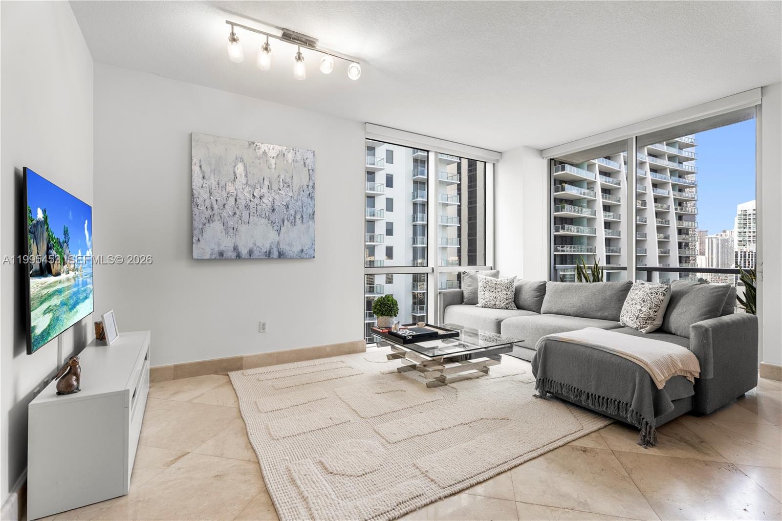 A modern living room features a grey sectional sofa, glass coffee table, and floor-to-ceiling windows — 1060 Brickell Ave # 2117, Miami FL 33131, MIAMI, FL