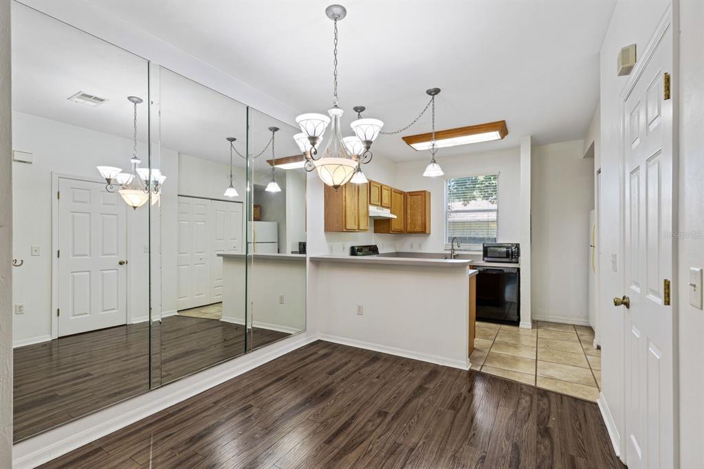 A dining area with a mirrored wall, wood-look flooring, and a chandelier adjacent to a kitchen — 3552 SW 30TH WAY UNIT 138, GAINESVILLE, FL