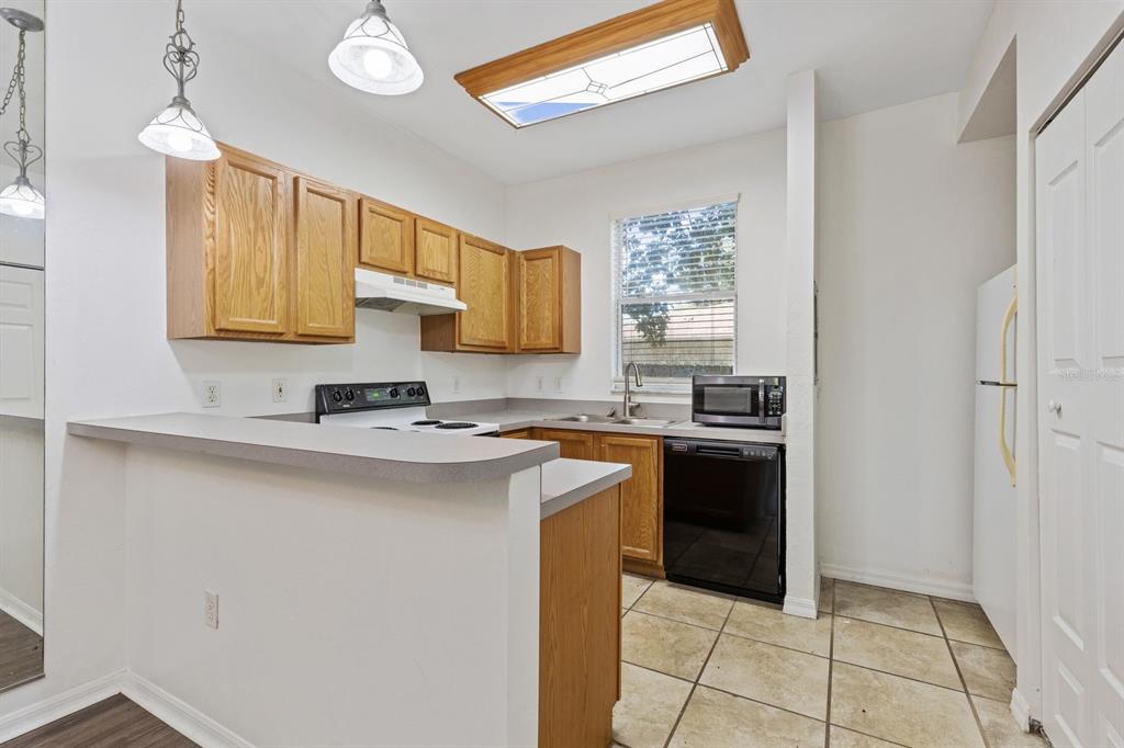 A kitchen features oak cabinets, a breakfast bar, tile flooring, and a black dishwasher — 3552 SW 30TH WAY UNIT 138, GAINESVILLE, FL