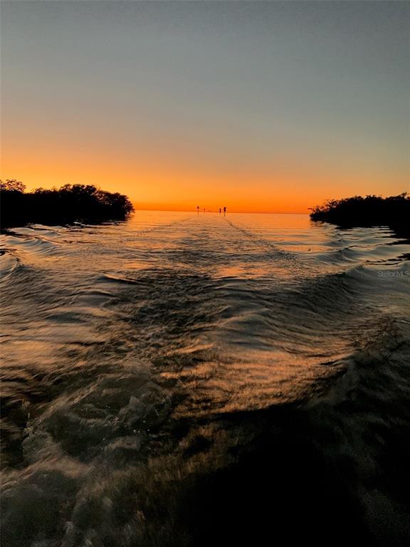 A boat wake flows through a channel between mangrove shorelines during a vibrant orange sunset — 7436 YACHTSMAN DRIVE, HUDSON, FL