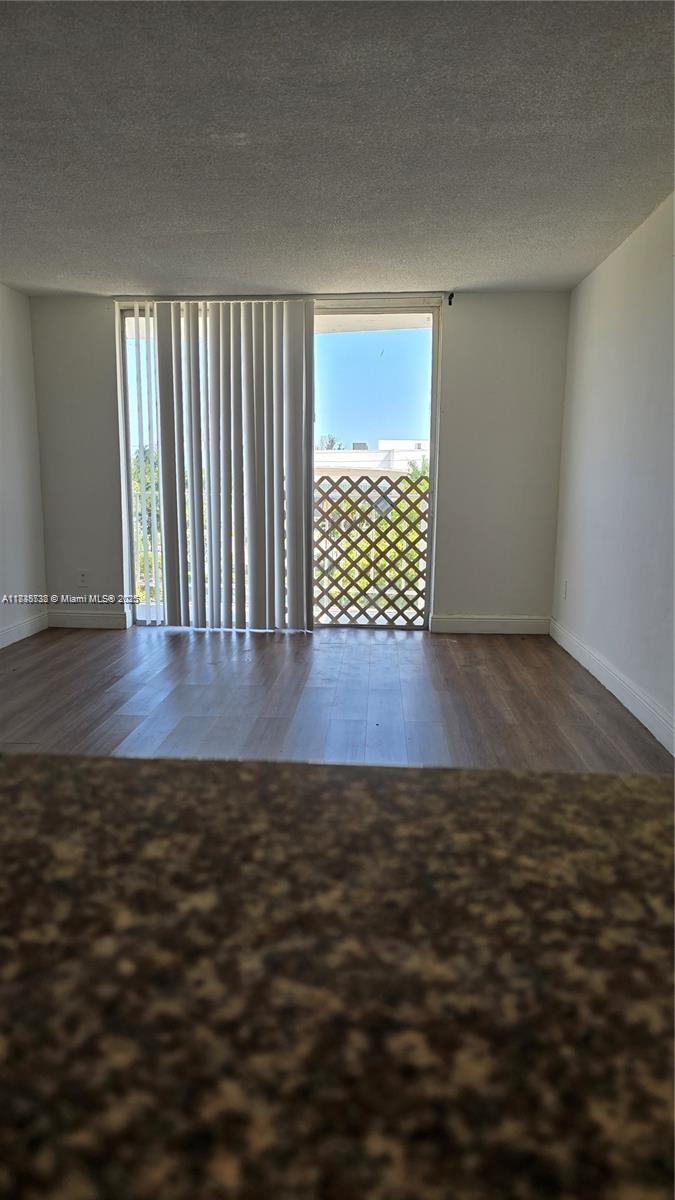 An empty room features wood-look flooring, vertical blinds, and a balcony with a lattice railing — 498 NW 165th St Rd # 407, Miami FL 33169, MIAMI, FL