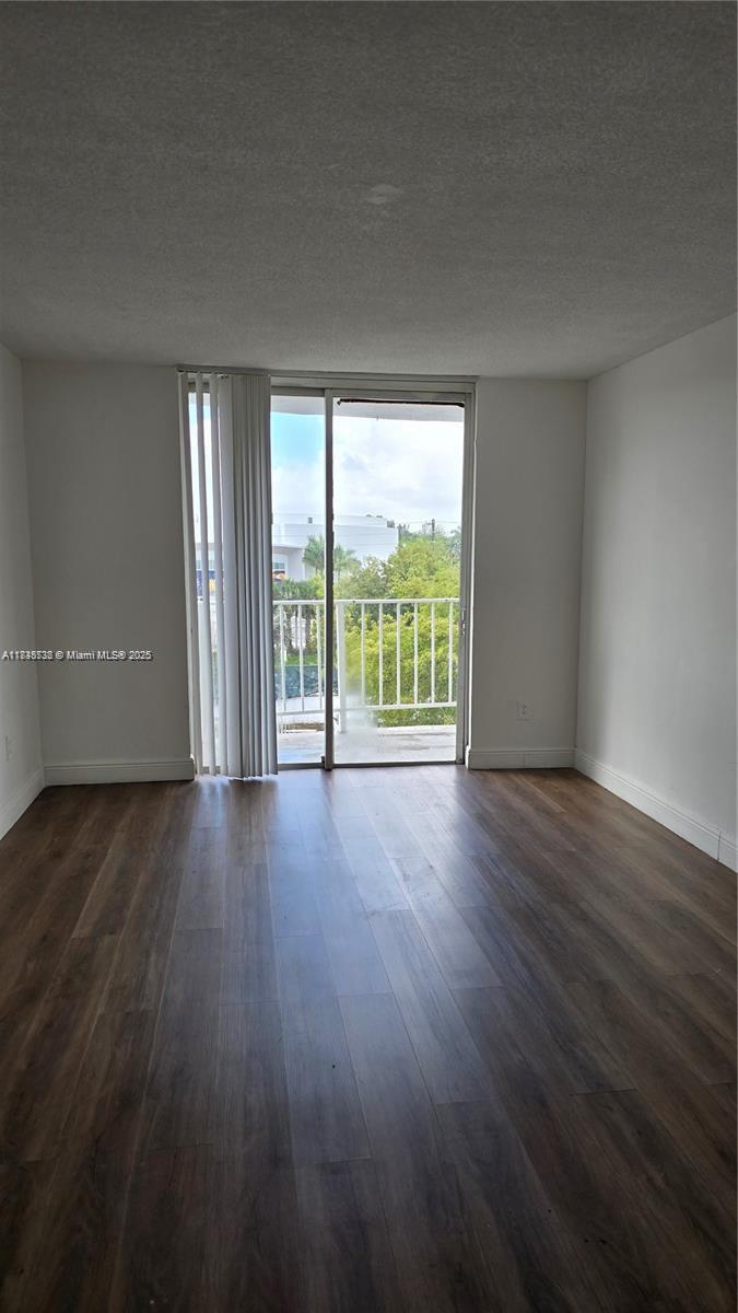 An empty room features wood-look flooring, white walls, and a sliding glass door to a balcony — 498 NW 165th St Rd # 407, Miami FL 33169, MIAMI, FL
