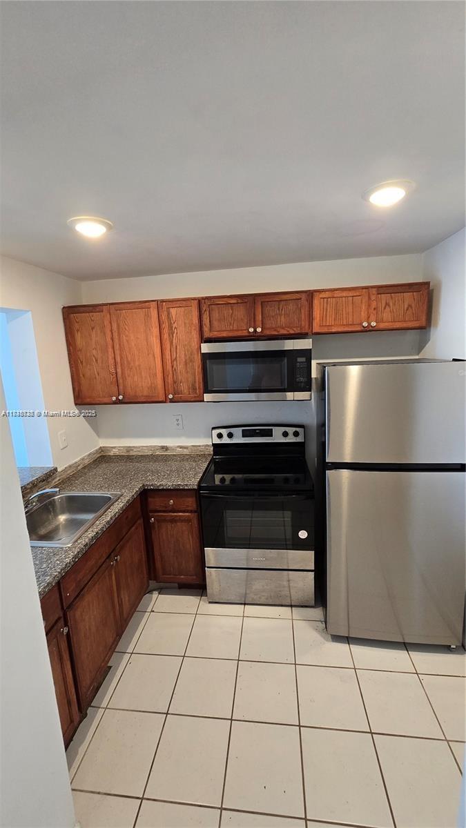 A kitchen features wood cabinets, stainless steel appliances, granite countertops, and white tile flooring — 498 NW 165th St Rd # 407, Miami FL 33169, MIAMI, FL