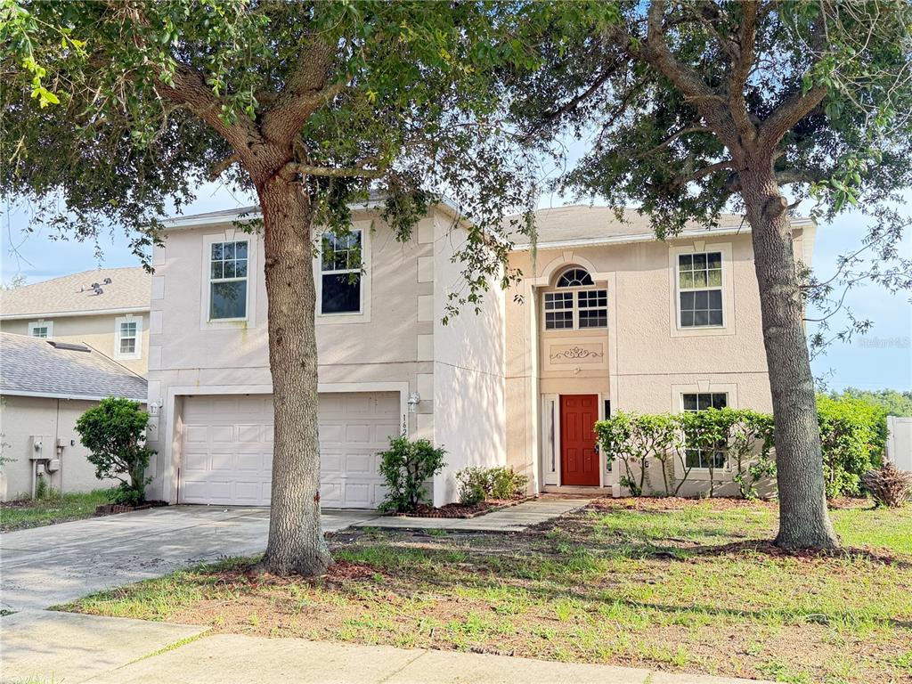 A two-story house with a beige stucco exterior, a two-car garage, and a red door — 1624 STERNS DRIVE, LEESBURG, FL