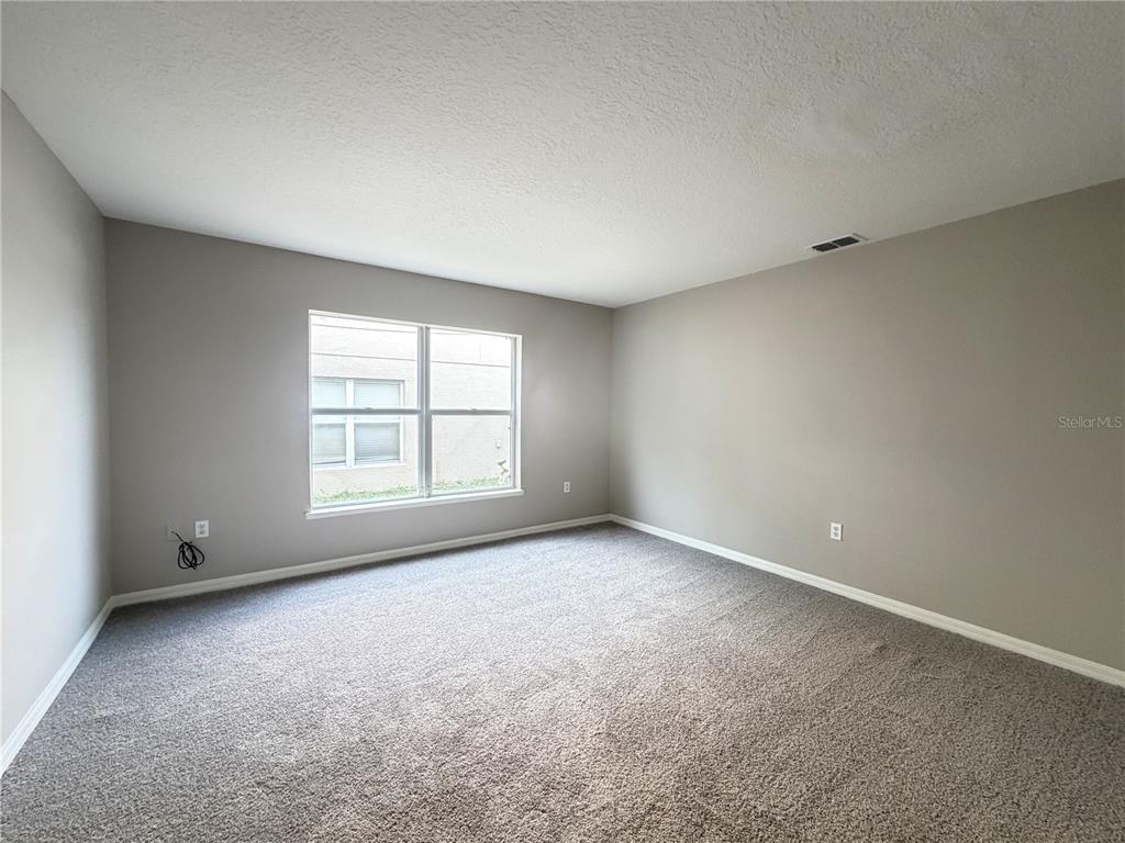 An empty bedroom features gray walls, beige carpeting, and a large window — 1624 STERNS DRIVE, LEESBURG, FL