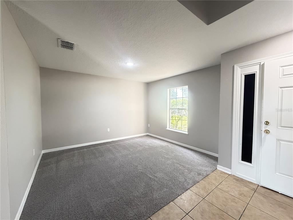 An empty room features gray carpet, light gray walls, a single window, and a white door — 1624 STERNS DRIVE, LEESBURG, FL