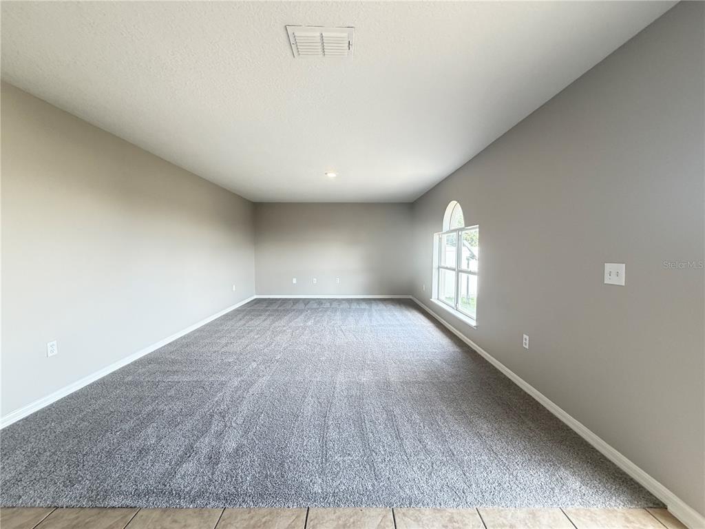 An empty room features gray walls, gray carpeting, and a large arched window — 1624 STERNS DRIVE, LEESBURG, FL