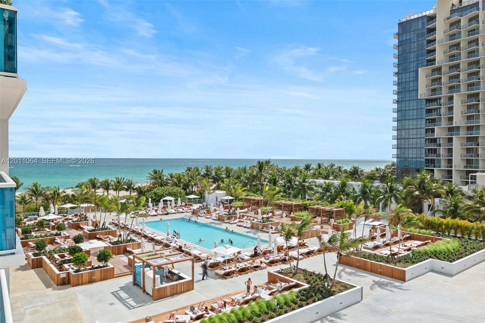 An elevated view shows a resort-style swimming pool surrounded by lounge chairs and palm trees — 2301 Collins Ave # 504, Miami Beach FL 33139, MIAMI BEACH, FL