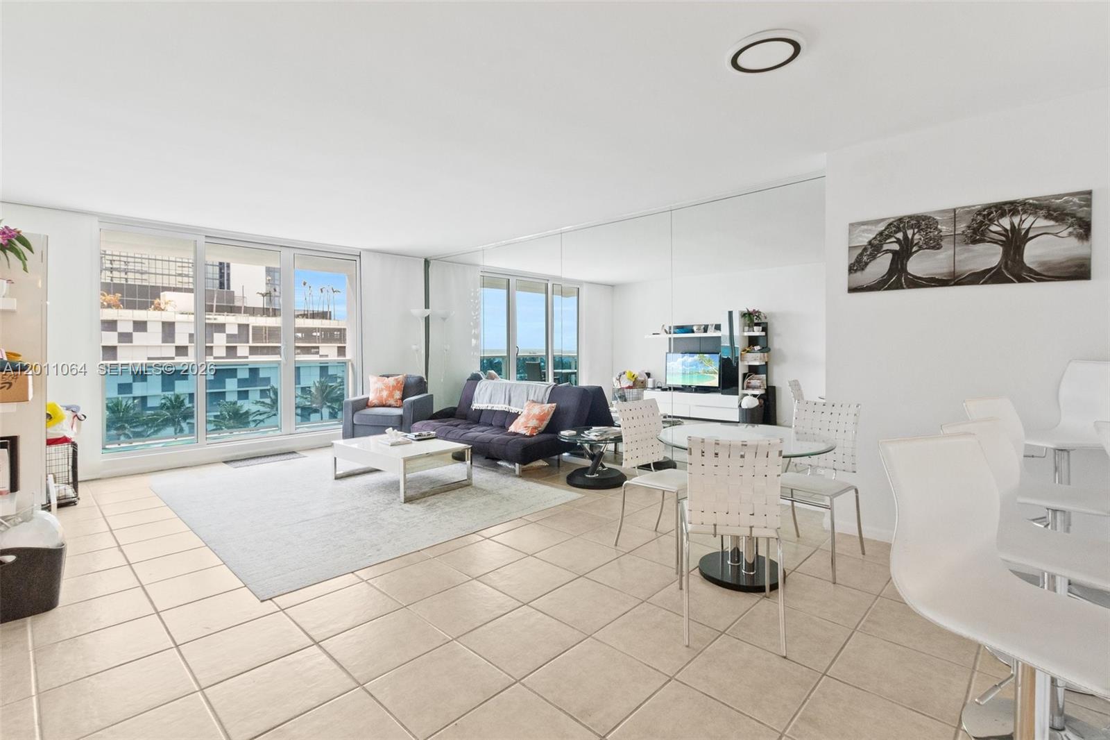 A living and dining area with tile floors, mirrored walls, and floor-to-ceiling windows — 2301 Collins Ave # 504, Miami Beach FL 33139, MIAMI BEACH, FL