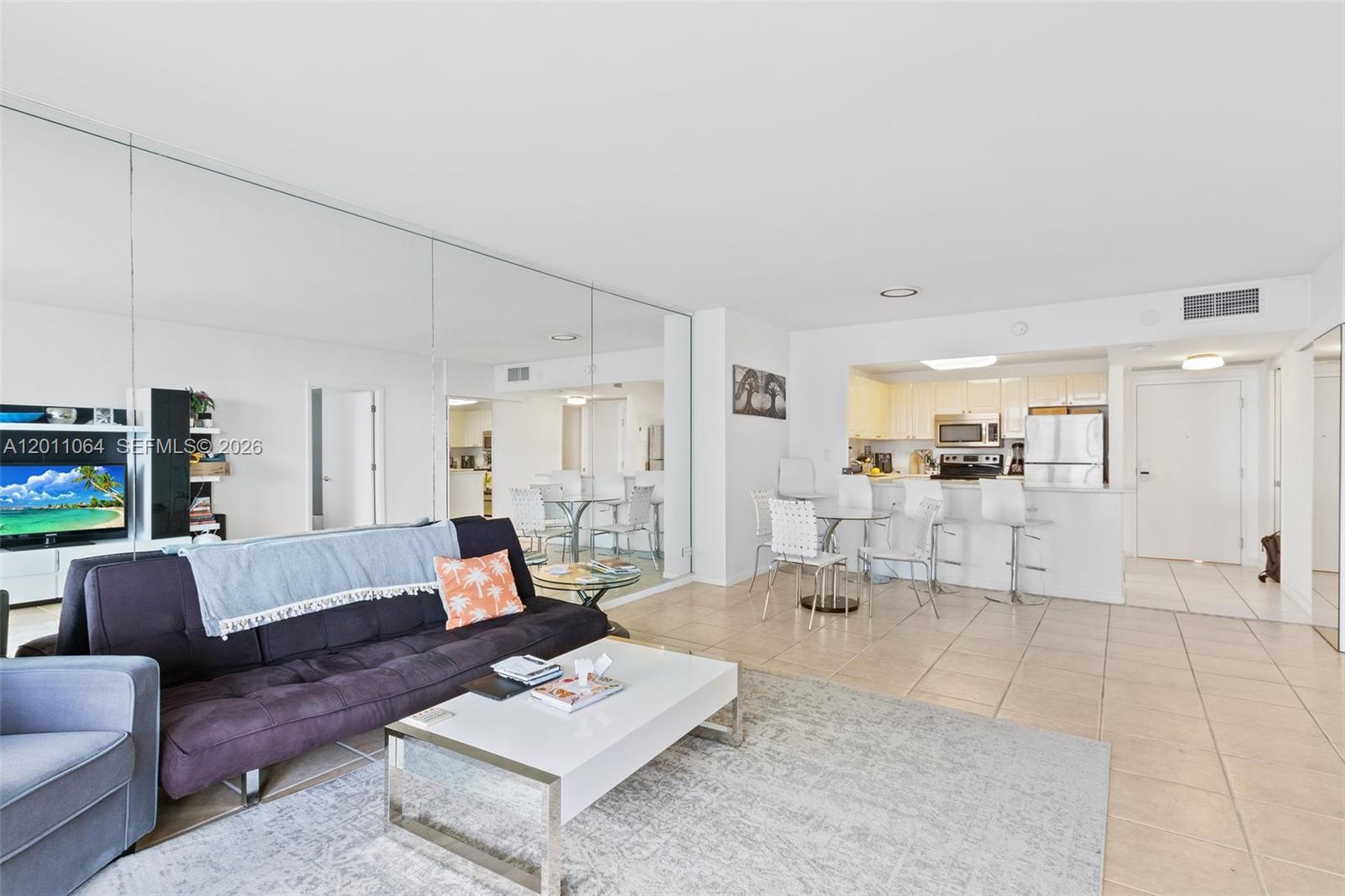 A living room with a mirrored wall, tile floors, and an open kitchen area — 2301 Collins Ave # 504, Miami Beach FL 33139, MIAMI BEACH, FL
