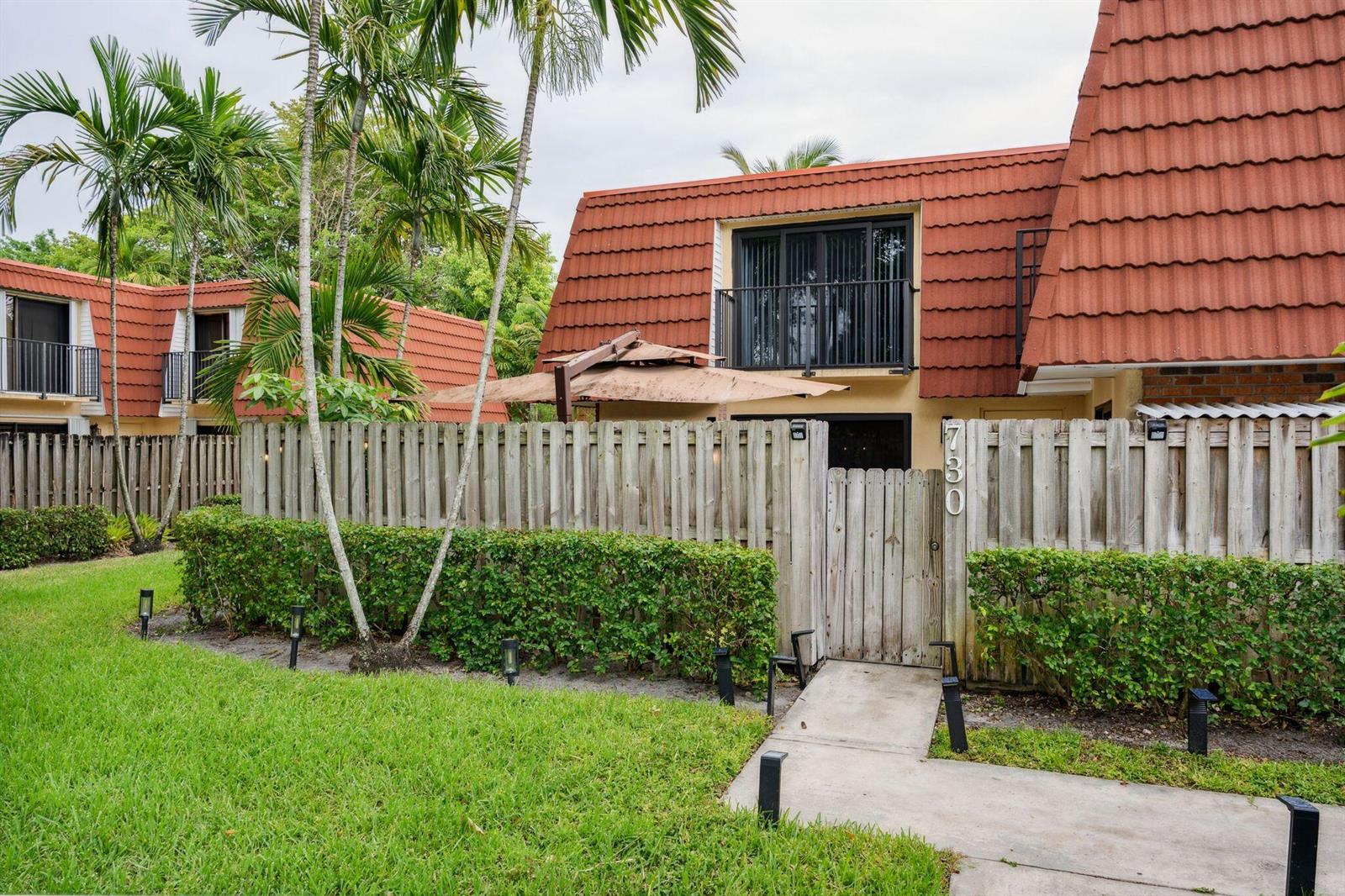 A two-story townhouse with a red tile roof, wooden privacy fence, and a small patio — 730 NW 99th Circle, Plantation FL 33324, PLANTATION, FL