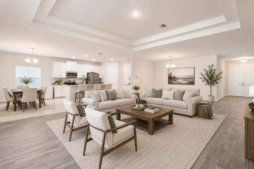 An open-concept living room and kitchen with white cabinetry, neutral furniture, and light wood flooring — 523 BELLISSIMO PLACE, HOWEY IN THE HILLS, FL