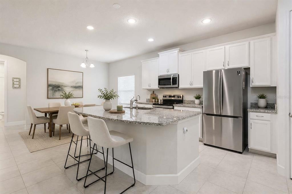 A kitchen with white cabinets, granite countertops, stainless steel appliances, and an island with stools — 523 BELLISSIMO PLACE, HOWEY IN THE HILLS, FL