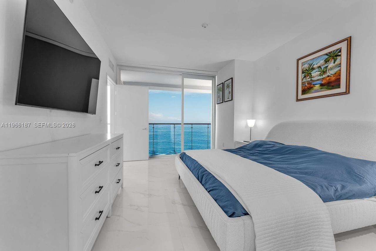 A bedroom features a white dresser, a bed with blue bedding, and a balcony view — 700 NE 24th St # 1405, Miami FL 33137, MIAMI, FL