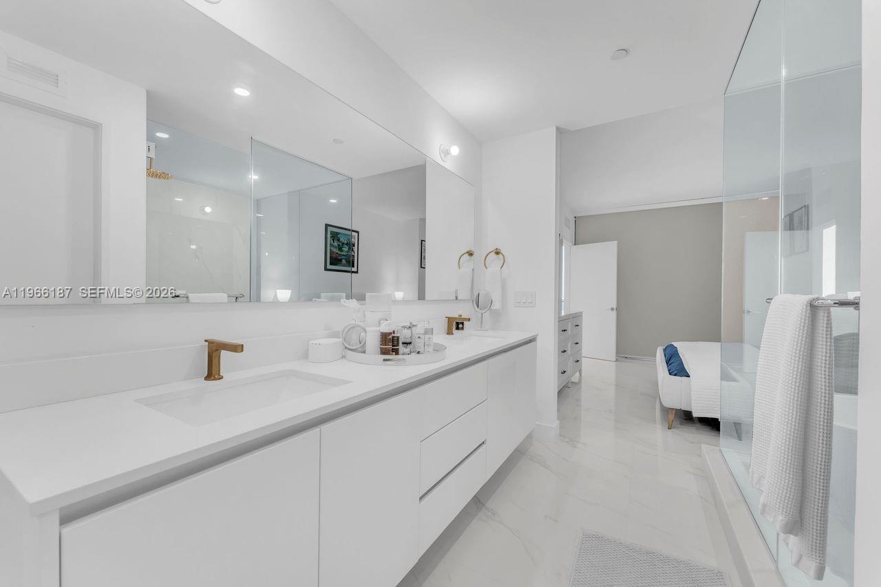 A modern white bathroom features a double vanity with gold faucets and a glass shower — 700 NE 24th St # 1405, Miami FL 33137, MIAMI, FL