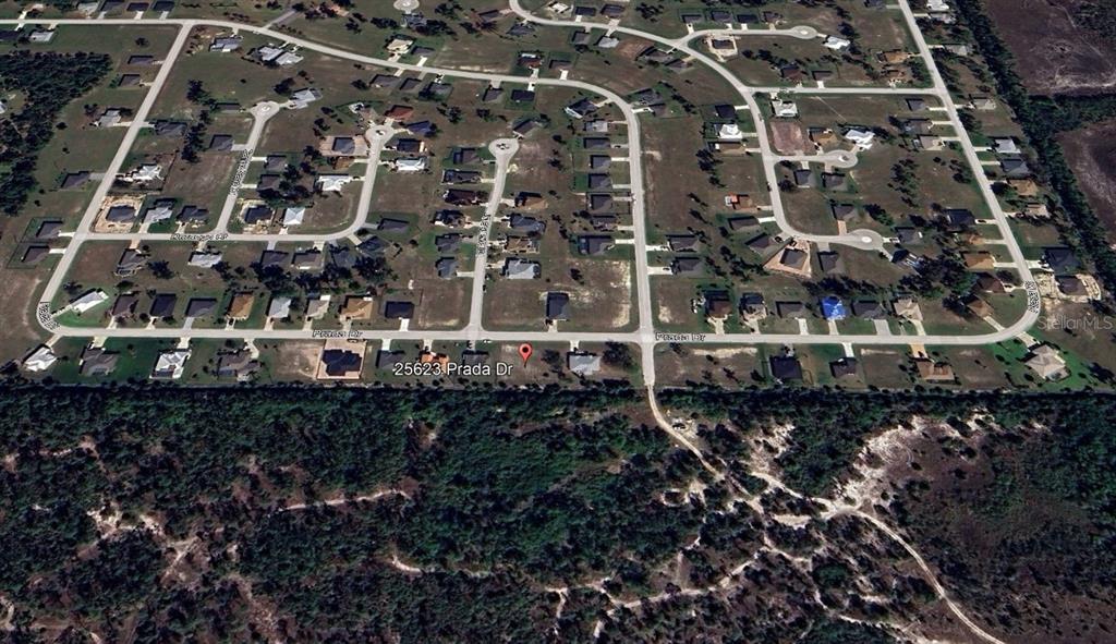 An aerial view shows a suburban neighborhood with single-family homes and surrounding wooded areas — 25623 PRADA DRIVE, PUNTA GORDA, FL