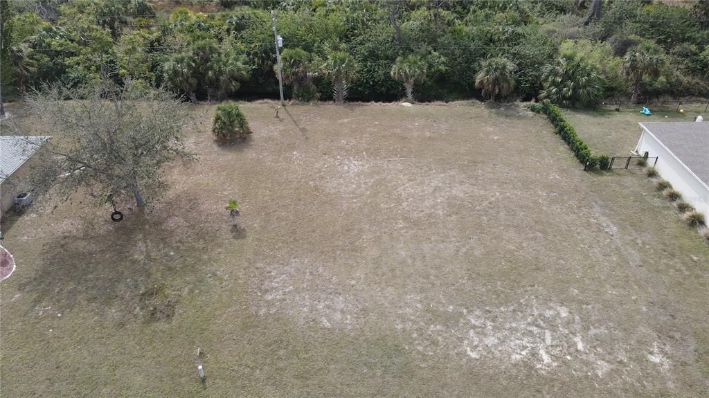 An aerial view shows a large, vacant grassy lot bordered by trees and neighboring houses — 25623 PRADA DRIVE, PUNTA GORDA, FL