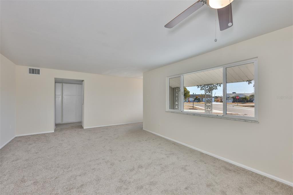 A carpeted living room features a ceiling fan, a large window, and a closet doorway — 703 BEL AIR AVENUE, SUN CITY CENTER, FL