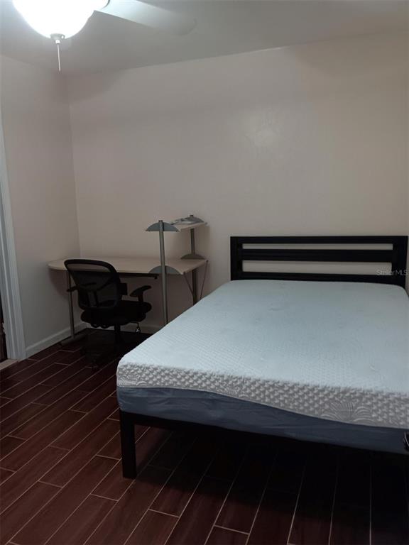A bedroom features a bed, a desk with a chair, and dark wood-look tile flooring — 4000 SW 23RD STREET UNIT 4-308, GAINESVILLE, FL