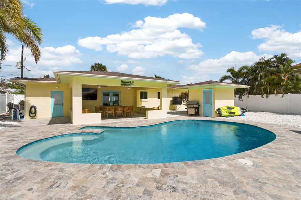 A swimming pool sits in front of a yellow house with a covered patio area — 517 39TH AVENUE, ST PETE BEACH, FL