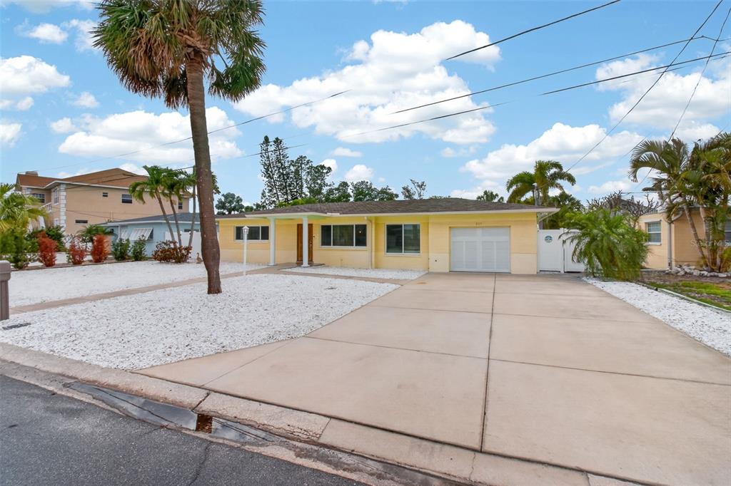 A single-story yellow house features a concrete driveway, a white gravel yard, and palm trees — 517 39TH AVENUE, ST PETE BEACH, FL