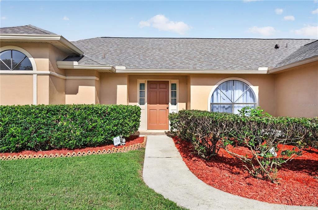 A tan house exterior features a brown front door, arched windows, and manicured hedges — 4059 WATERVIEW LOOP, WINTER PARK, FL