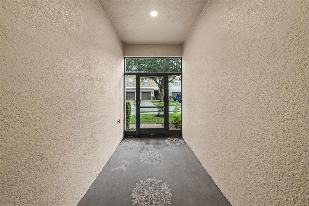 A covered entryway with textured beige walls, a concrete floor, and a glass storm door — 11927 GREENGATE DRIVE, HUDSON, FL