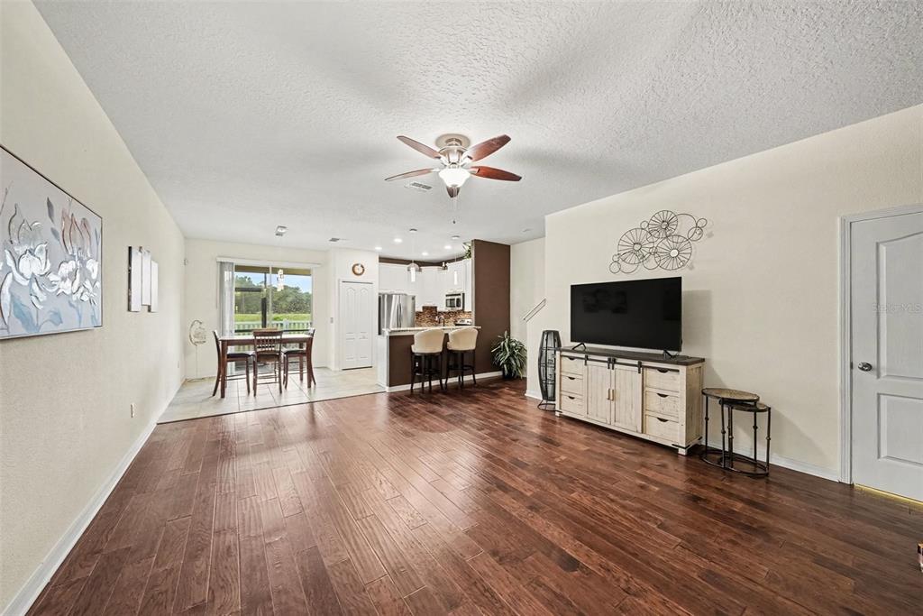 An open-concept living room and kitchen featuring dark wood flooring and a ceiling fan — 11927 GREENGATE DRIVE, HUDSON, FL