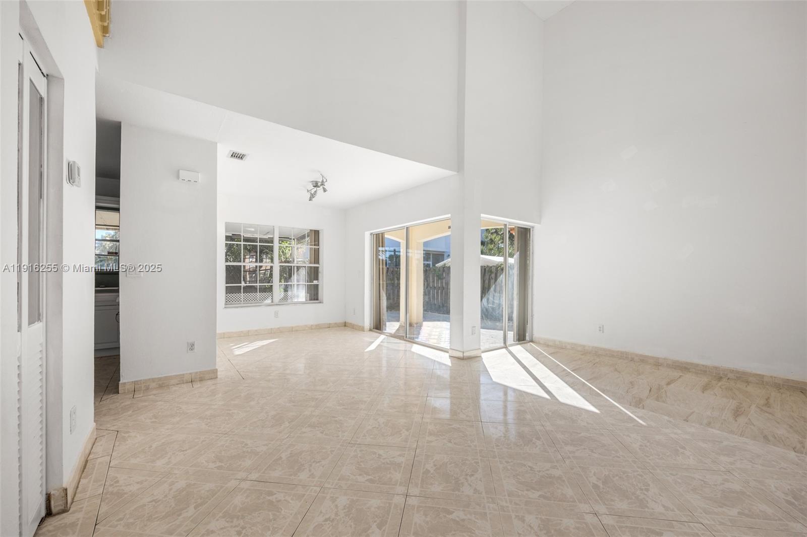 An empty room features high ceilings, tile flooring, large windows, and sliding glass patio doors — 9162 SW 213th Ln, Cutler Bay FL 33189, CUTLER BAY, FL