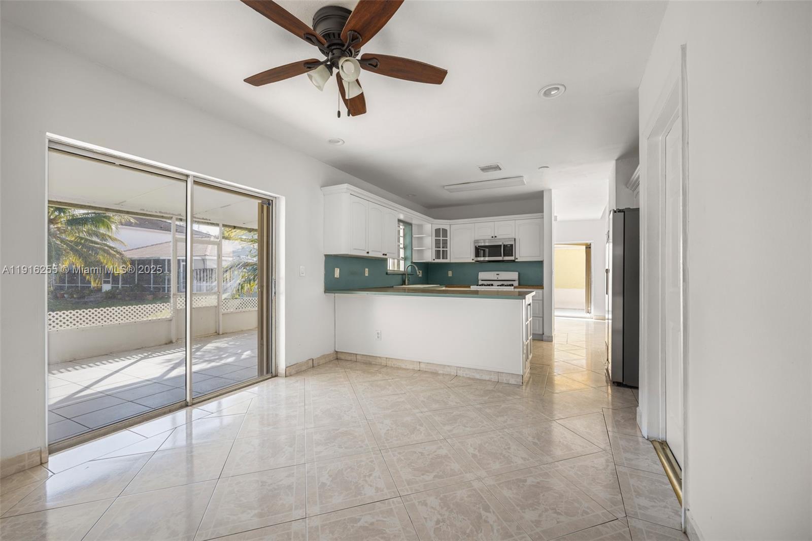 A kitchen with white cabinets and a tile floor opens to a covered patio — 9162 SW 213th Ln, Cutler Bay FL 33189, CUTLER BAY, FL
