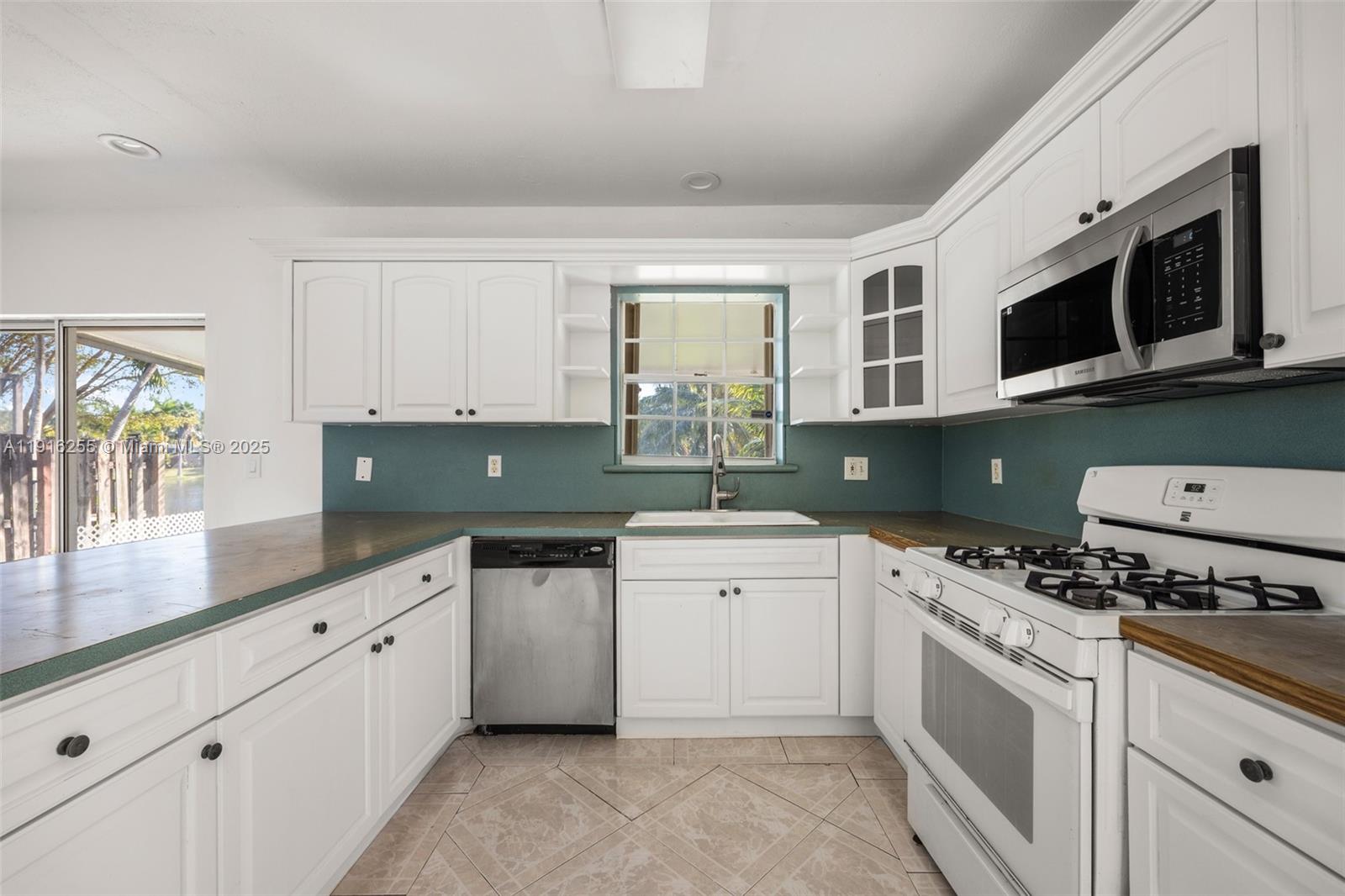 A kitchen features white cabinets, a teal backsplash, stainless steel appliances, and tile flooring — 9162 SW 213th Ln, Cutler Bay FL 33189, CUTLER BAY, FL