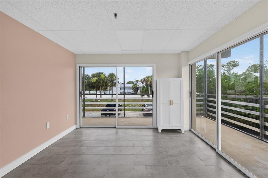 A room with gray tile flooring, a pink accent wall, and two sliding glass balcony doors — 1460 S MCCALL ROAD UNIT A1, ENGLEWOOD, FL