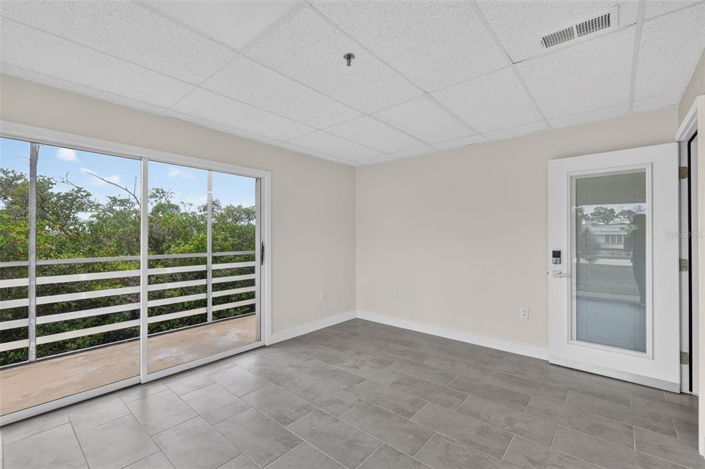 An empty room with gray tile flooring, a drop ceiling, sliding glass doors, and a door — 1460 S MCCALL ROAD UNIT A1, ENGLEWOOD, FL