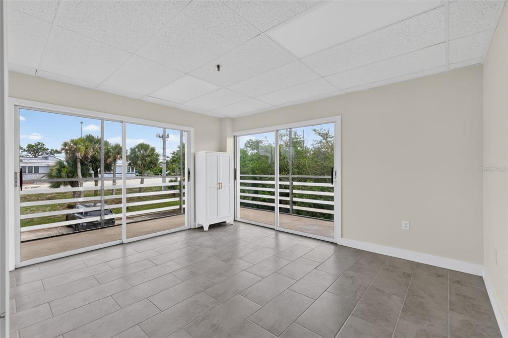 An empty room with gray tile floors, a drop ceiling, and two sliding glass doors — 1460 S MCCALL ROAD UNIT A1, ENGLEWOOD, FL