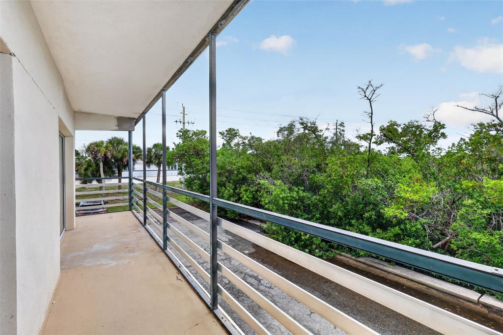 A balcony with a metal railing overlooks a parking area and dense green trees — 1460 S MCCALL ROAD UNIT A1, ENGLEWOOD, FL