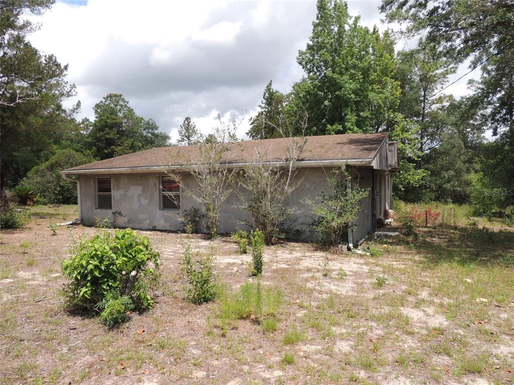 A single-story house with a stucco exterior sits on a sandy, overgrown lot — 11351 SE 32ND PLACE, MORRISTON, FL