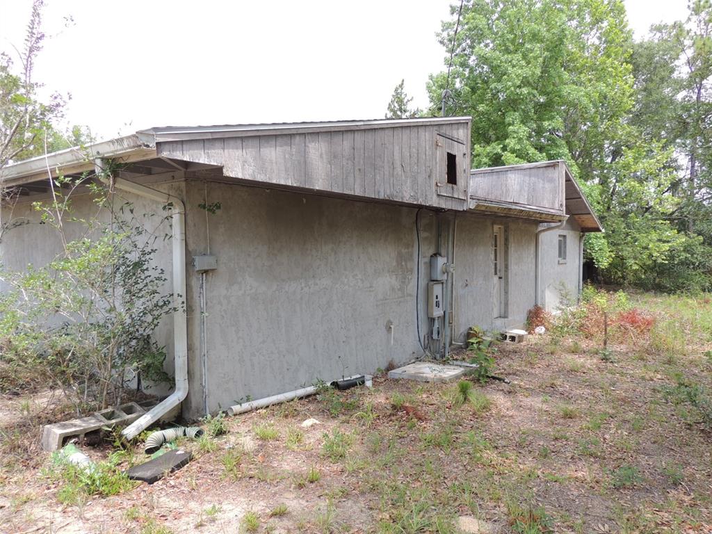 The exterior of a single-story house features a stucco wall, wood siding, and a downspout — 11351 SE 32ND PLACE, MORRISTON, FL